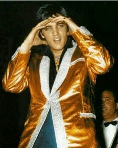 elvis presley in gold jacket holding his hands up to his face and looking into the distance