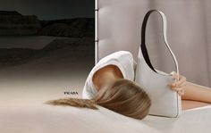 a woman laying on top of a bed next to a white purse with her head resting on the pillow