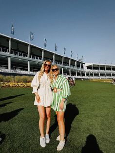two women standing in the grass at a race track with their arms around each other