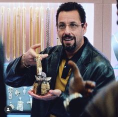 a man in glasses is holding up a gold bracelet and pointing to it with his finger