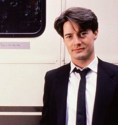 a man wearing a suit and tie standing in front of a bus