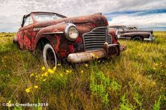 an old rusted car sitting in the middle of a field