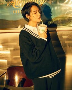 a young man drinking from a cup while standing in front of a wall with an advertisement behind him
