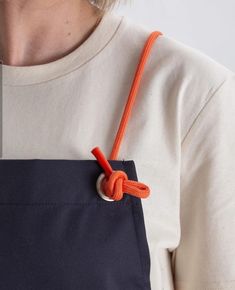 a woman wearing an orange rope around her neck and holding onto a black apron with white buttons