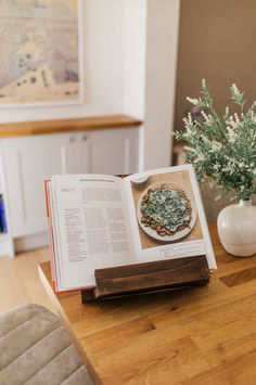 an open book sitting on top of a wooden table next to a vase filled with flowers