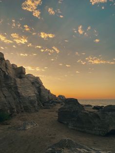 the sun is setting over some rocks on the beach