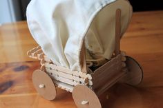 a small wooden toy carriage with a white cloth on it's back and wheels