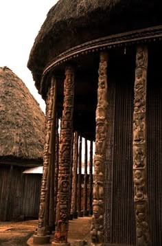 an old building with many pillars and thatched roof tops in front of some huts