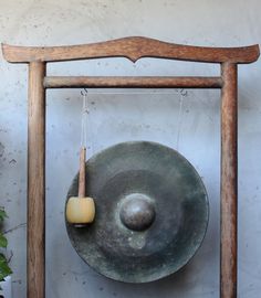 an old metal gong hanging from a wooden frame on a wall next to a potted plant