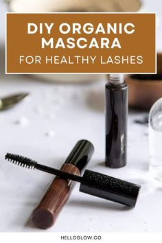 Close-up of natural mascara tubes and brushes placed on a white surface with scattered cosmetic ingredients.