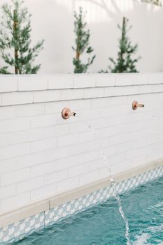 two faucets are connected to the side of a white brick wall with water running from them