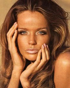 a woman with long brown hair and blue eyes posing for a magazine cover, holding her hand to her face