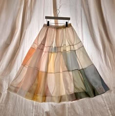 a skirt hanging on a hanger in front of a white curtain with multicolored squares
