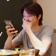 a woman sitting at a table looking at her cell phone while eating food with chopsticks in front of her