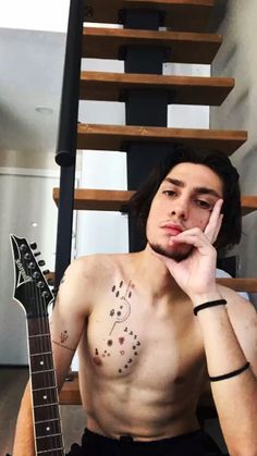 a shirtless man sitting next to a guitar