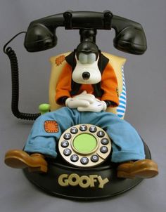 an old fashioned rotary telephone with goofy sitting on it's base and holding a cell phone up to its ear