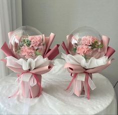 two clear vases with pink flowers in them sitting on a white tablecloth covered surface