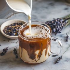 a pitcher pouring milk into a mug filled with liquid and lavenders next to it