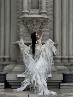 a woman dressed in white feathers sitting on a stone fountain with her arms spread out