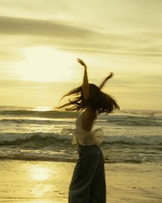 a woman standing on top of a sandy beach next to the ocean with her arms in the air