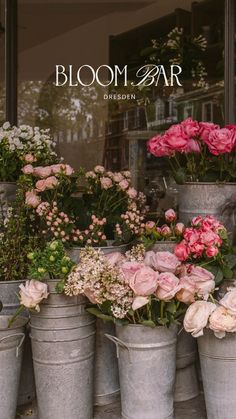 several buckets filled with pink flowers sitting in front of a flower shop window that says bloom bar