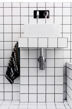a white sink sitting next to a mirror on a tiled bathroom wall with black and white tiles