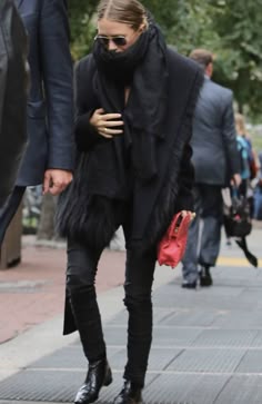 a woman in black is walking down the street with her hand on her hip and wearing a scarf