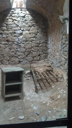 an old stone building with a bed and shelf in the corner, next to a window
