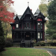 an old victorian style house with red trim and black roof, surrounded by trees in the fall
