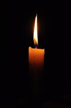 a lit candle in the dark with its light shining on it's side and black background