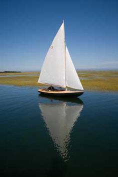 a sailboat floating on top of a lake next to a green grass covered field
