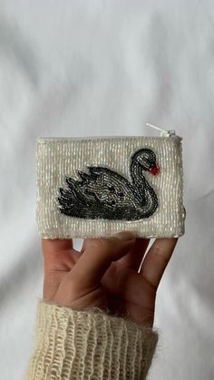 a hand holding a small white purse with a black swan on it's side