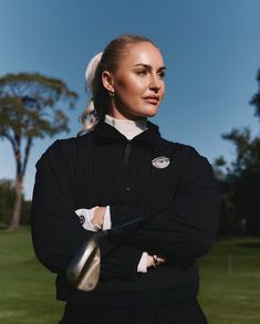 a woman with her arms crossed standing in front of a golf ball and club on the grass