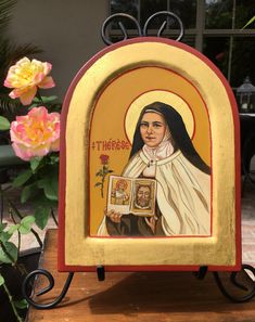 an icon of the mother of jesus is displayed in front of some flowers and a potted plant