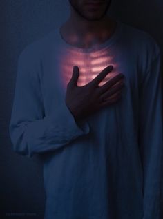 a man is holding his hand up to the light coming through his chest and hands on his chest