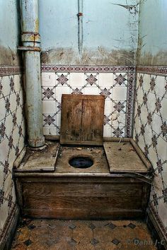 an old wooden toilet in the corner of a room with tiled walls and flooring
