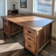 a wooden desk sitting in front of a window next to a lamp and pictures on the wall