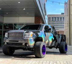 a silver truck with purple and blue wheels parked in front of a building on the street
