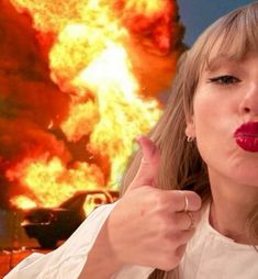 the woman is pointing to her lips in front of a large fire and flames behind her