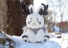 a stuffed animal with antlers sitting on top of snow covered ground next to a tree