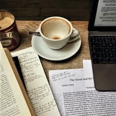 an open book next to a cup of coffee and a laptop on a wooden table