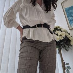 white frilly blouse with leather belt and silver buckle. checkered fitted trousers (high waisted) curly hair, rings, white