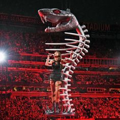 a woman standing on top of a giant snake in the middle of a stadium filled with people