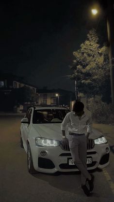 a man leaning on the hood of a white car in front of a street light