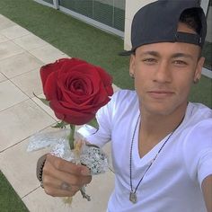 a man holding a red rose in his right hand and wearing a baseball cap on