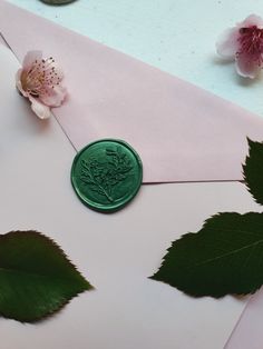 a green wax stamp sitting on top of an envelope next to pink flowers and leaves