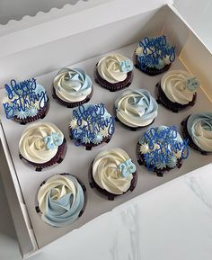 twelve cupcakes in a box with frosting and blue icing designs on them