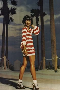 a woman standing in front of palm trees wearing high heeled sandals and a striped sweater