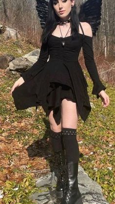 a woman in black dress and angel wings standing on rocks with her legs spread out