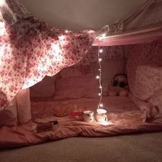 a pink bed with lights on it and some blankets in the corner, next to a teddy bear
